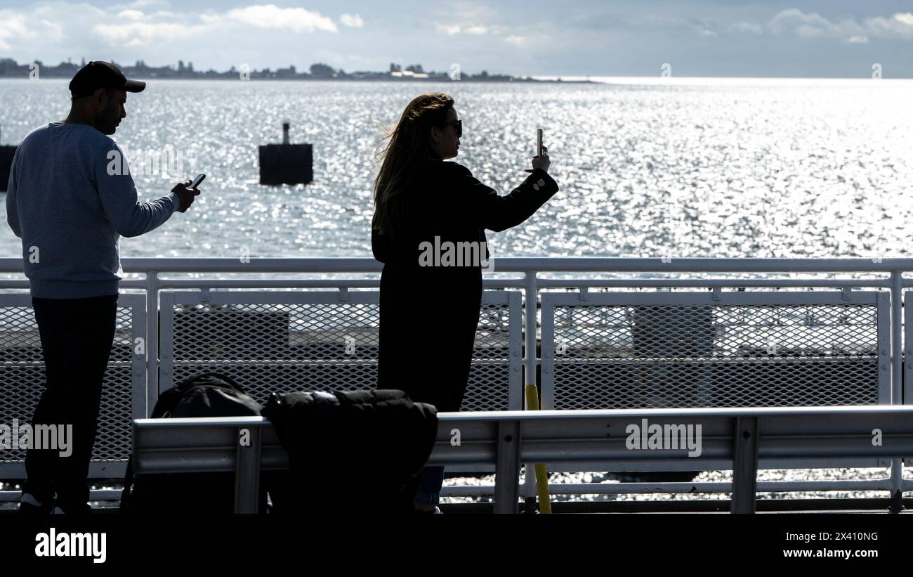 Les gens se tiennent debout photographiant l'océan chatoyant et la vue côtière avec leurs téléphones intelligents depuis le pont d'un traversier ; Colombie-Britannique, Canada Banque D'Images