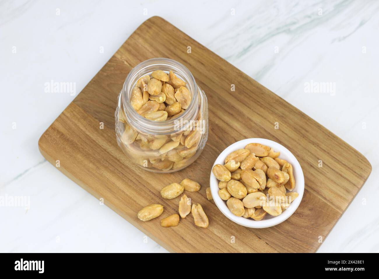 Kacang goreng ou cacahuètes frites dans un pot et une assiette blanche. Snack indonésien avec fond blanc marbre, mise au point sélective. Banque D'Images