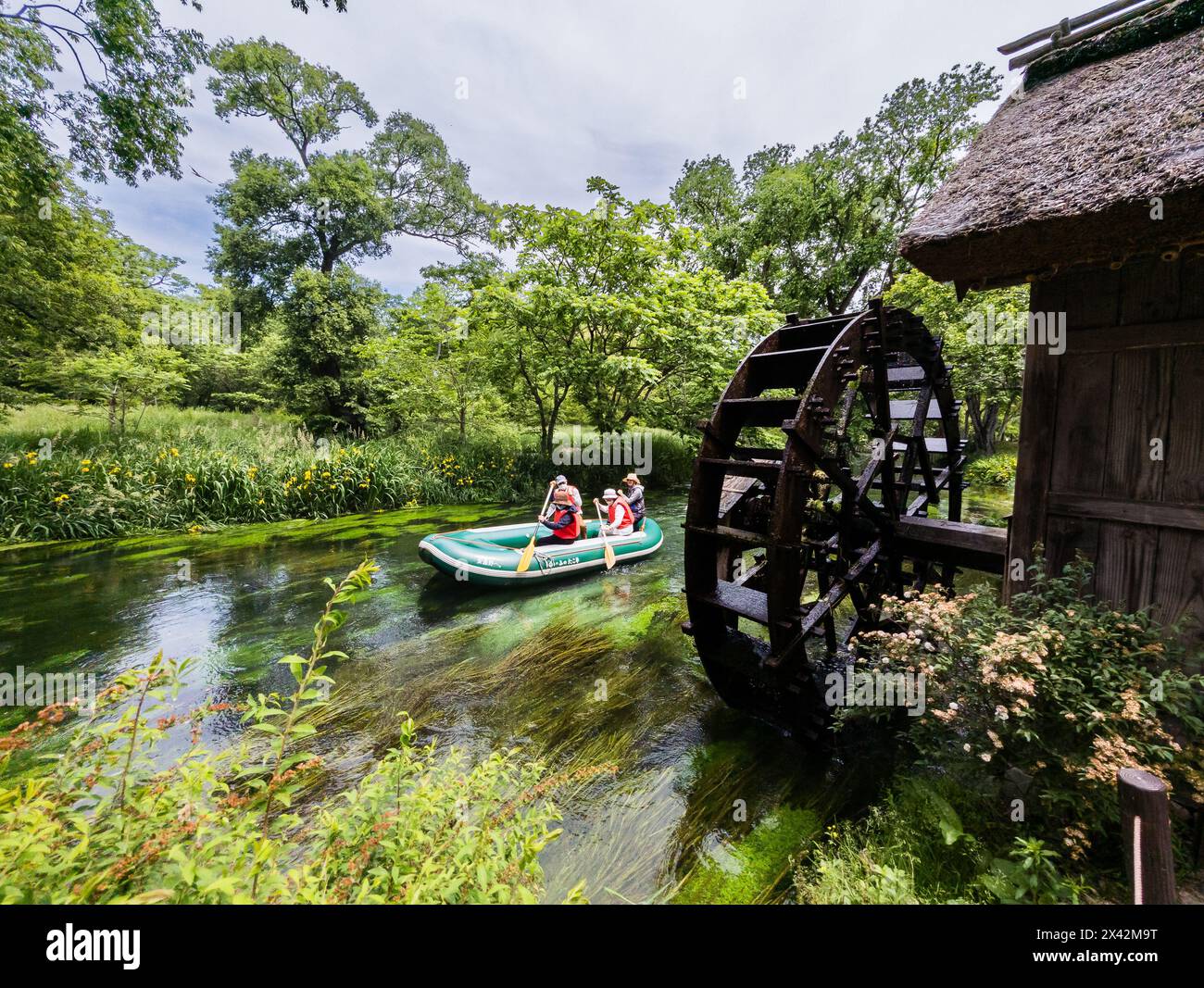 Touristes sur un petit bateau passant devant une vieille roue à eau traditionnelle sur une petite rivière à Nagano, Japon Banque D'Images