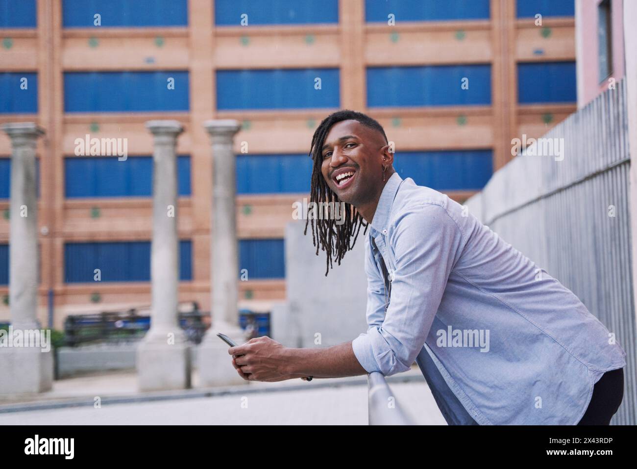 homme afro-américain souriant regardant dans la caméra avec son téléphone intelligent dans la main Banque D'Images