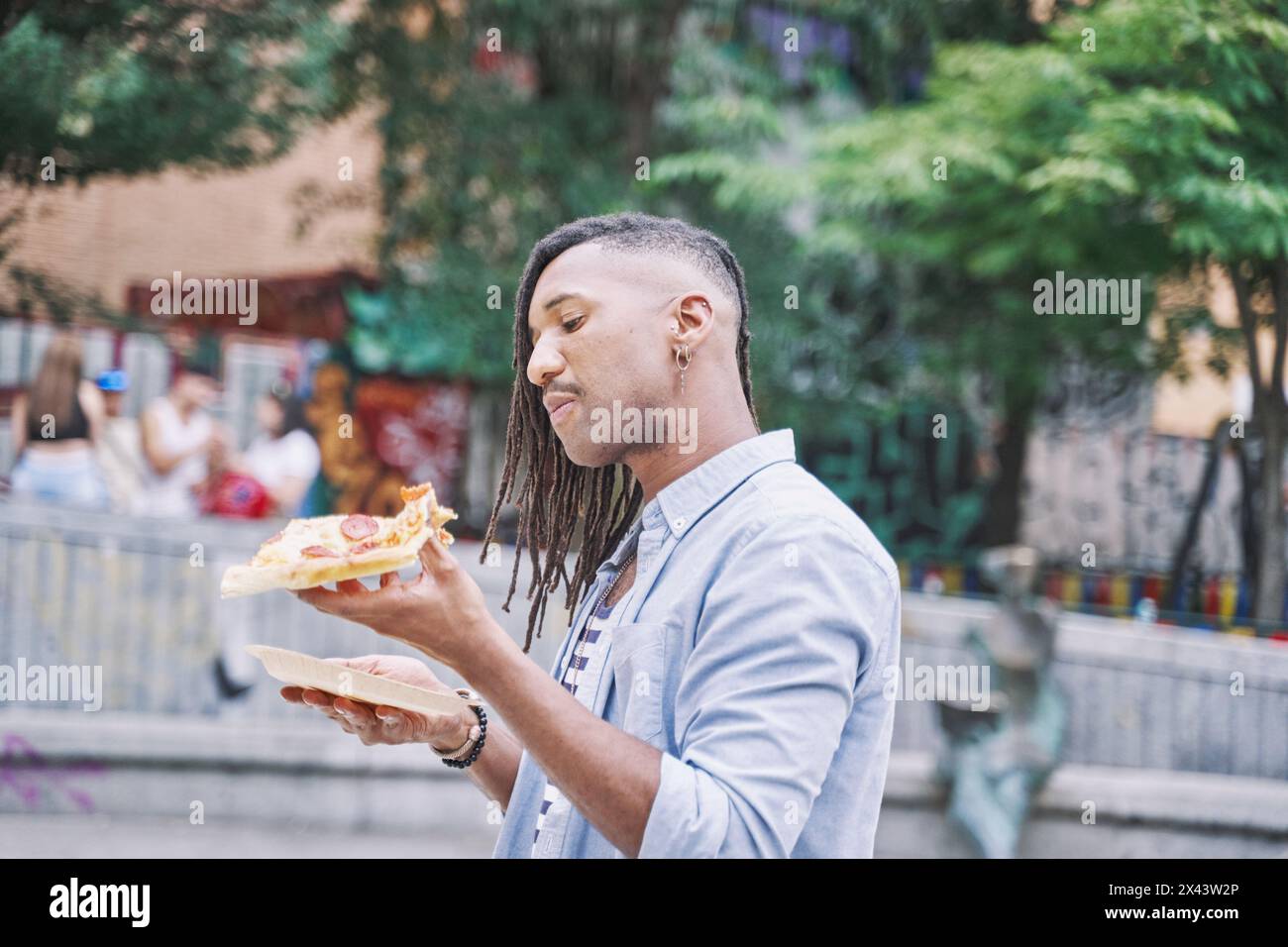 portrait d'un latin marchant à travers la ville mangeant une tranche de pizza. restauration rapide Banque D'Images