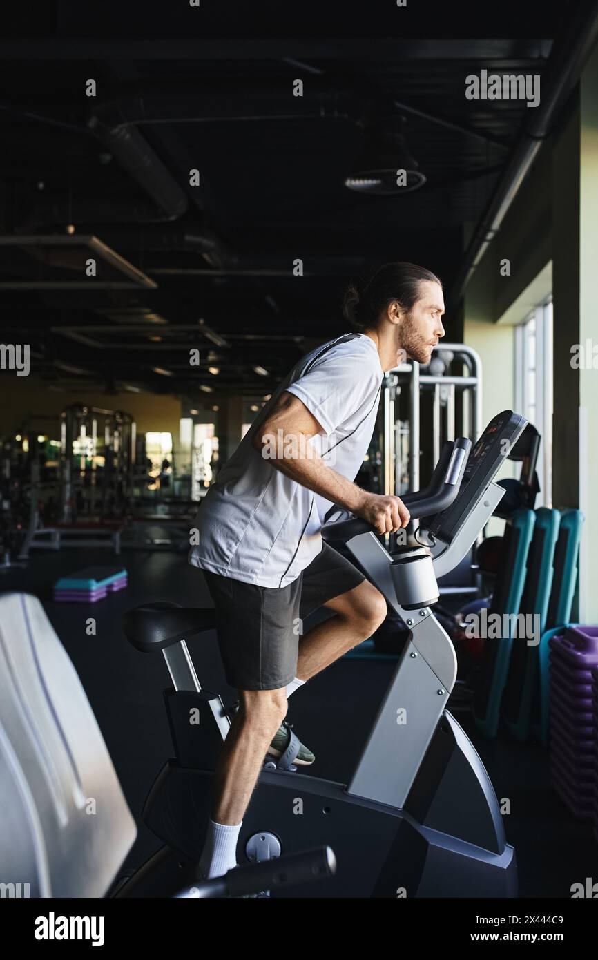 Homme musclé repoussant ses limites, sprint sur un vélo d'appartement dans un environnement de gymnastique moderne. Banque D'Images