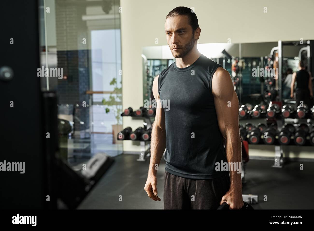 Un homme en tenue sportive se tient debout dans une salle de gym, tenant des plaques noires Banque D'Images