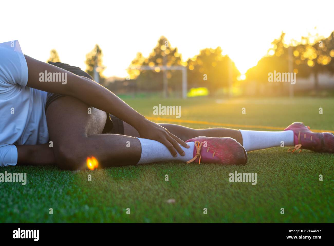 Joueur de football avec douleur à la jambe sur le terrain. Joueur de football allongé sur l'herbe frottant sa jambe. Joueur de football masculin allongé sur l'herbe frottant le sien Banque D'Images