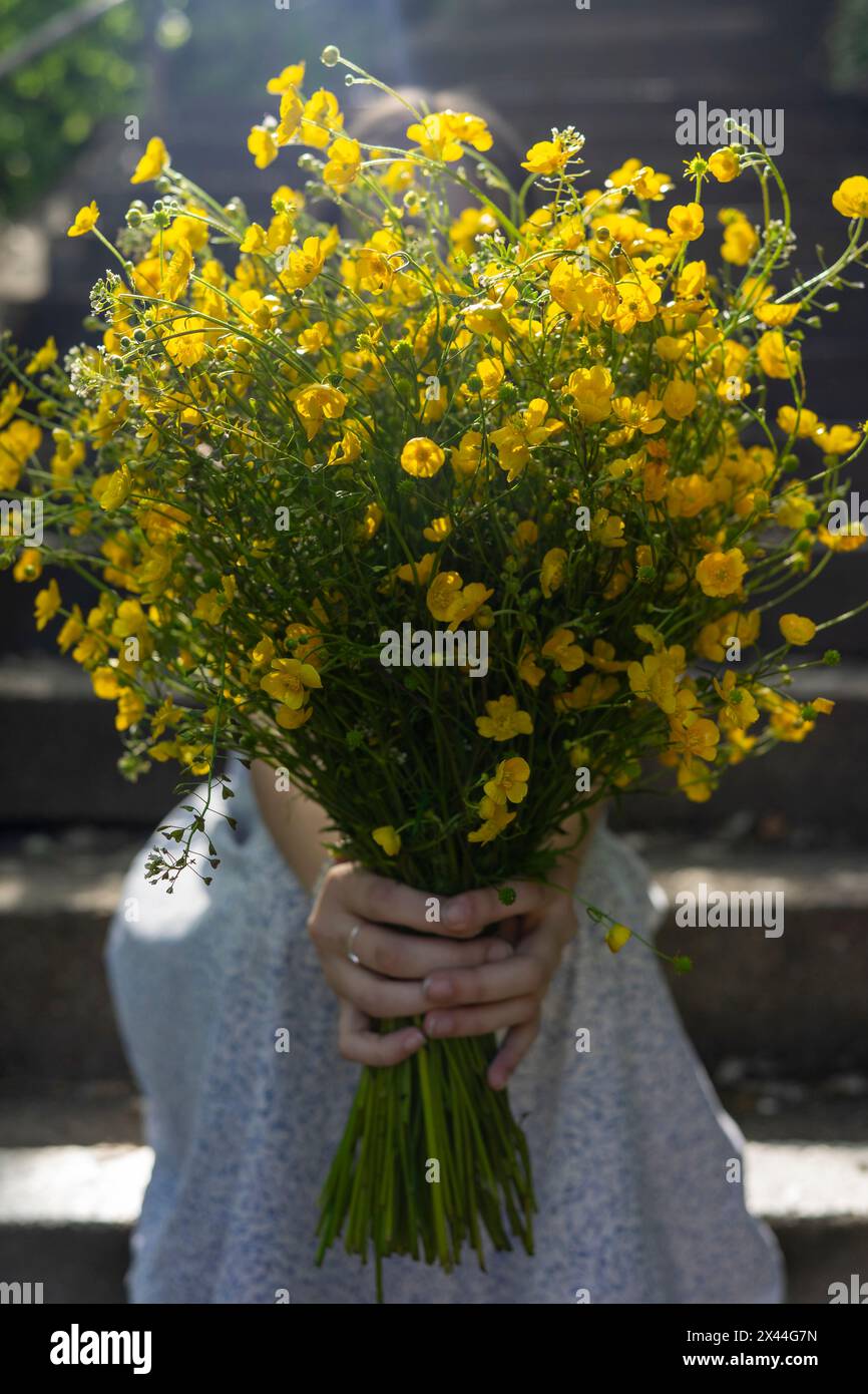 Fille ou femme avec de longs cheveux assis dans les escaliers avec un bouquet de fleurs jaunes en forme de papillon Banque D'Images