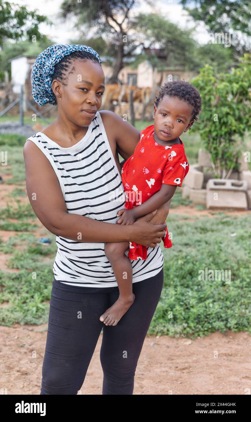 village africain , belle mère africaine célibataire tenant son enfant devant la maison dans la cour Banque D'Images