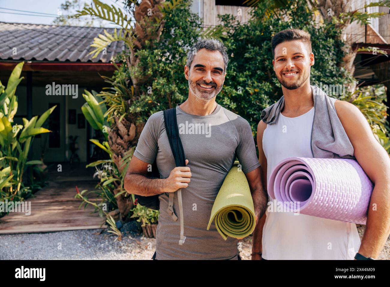 Portrait d'hommes souriants tenant des tapis de yoga tout en se tenant devant le centre de bien-être Banque D'Images