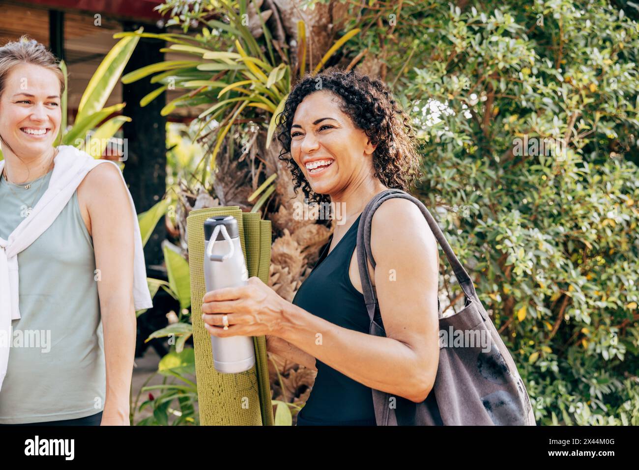 Femme heureuse tenant une bouteille d'eau tout en se tenant debout près d'une amie féminine à la station de bien-être Banque D'Images