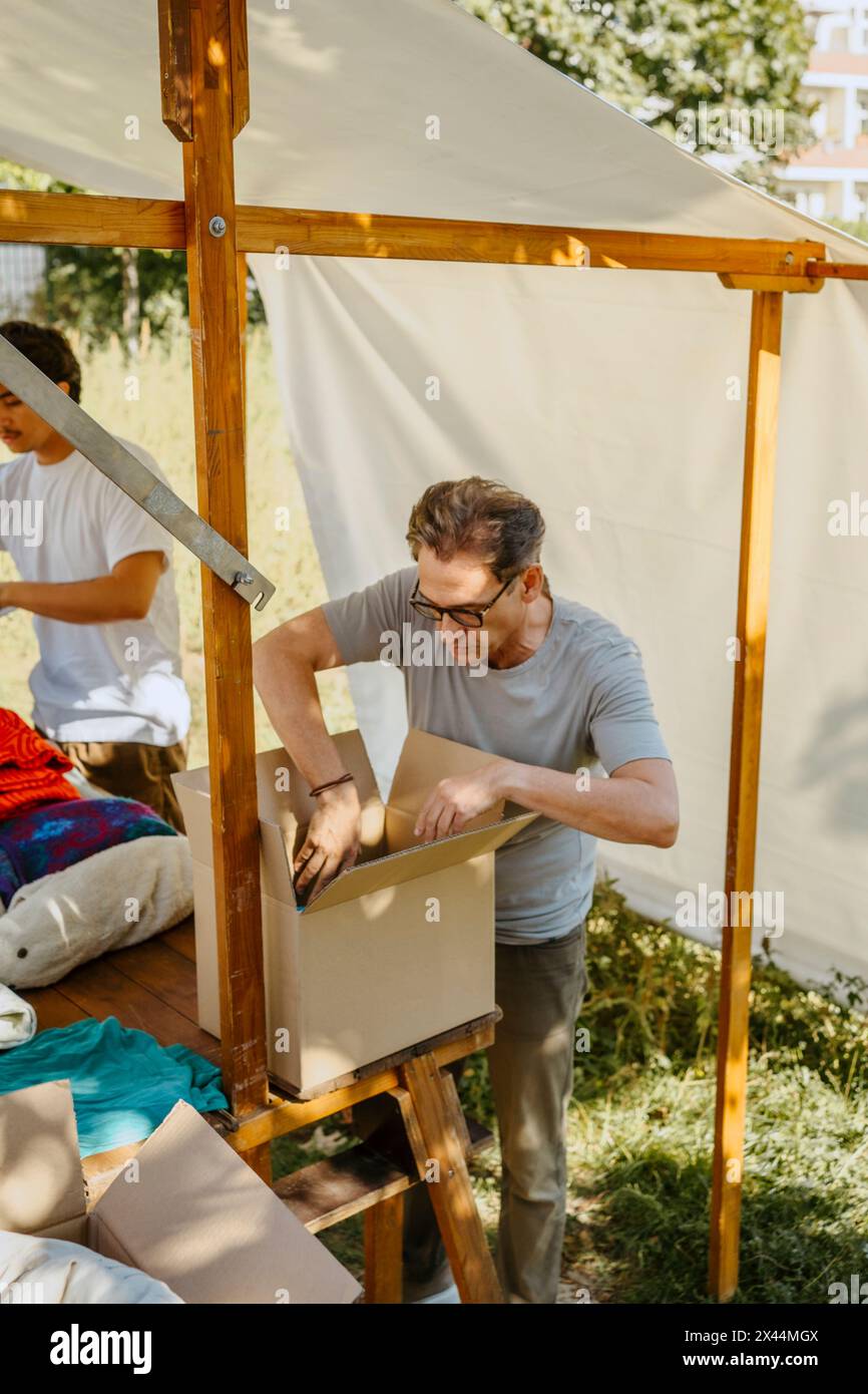 Bénévole masculin senior arrangeant des vêtements dans une boîte en carton sur la table pendant la campagne caritative au centre communautaire Banque D'Images