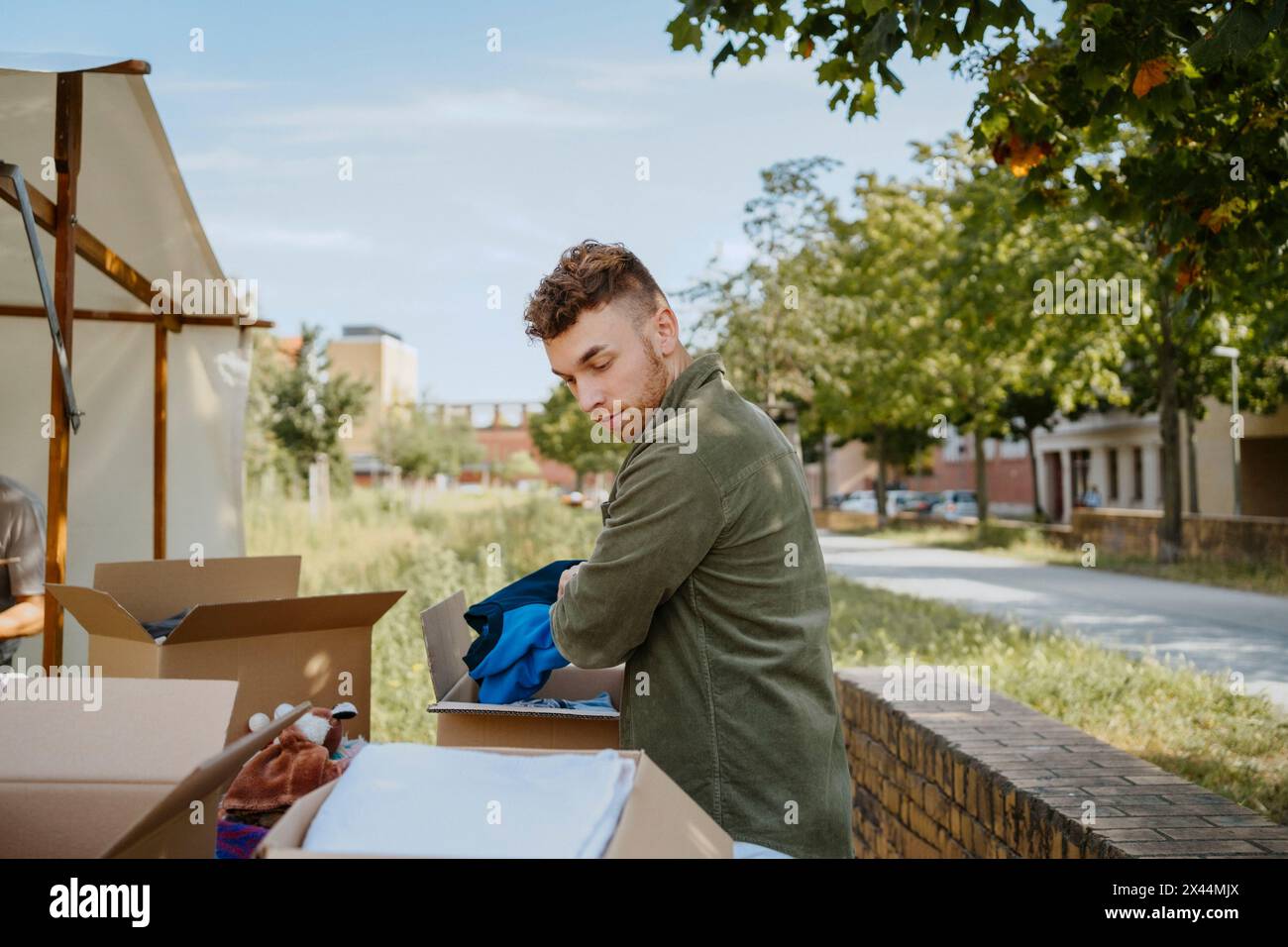 Vue latérale d'un jeune volontaire masculin emballant des vêtements dans des boîtes en carton tout en travaillant pendant une campagne caritative au cen communautaire Banque D'Images