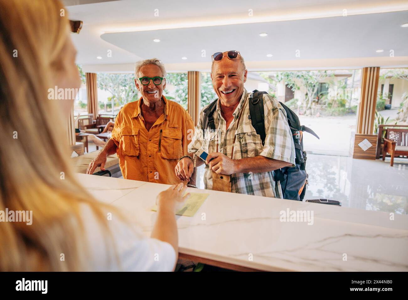 Heureux couple gay senior discutant avec une réceptionniste à la réception de l'hôtel Banque D'Images