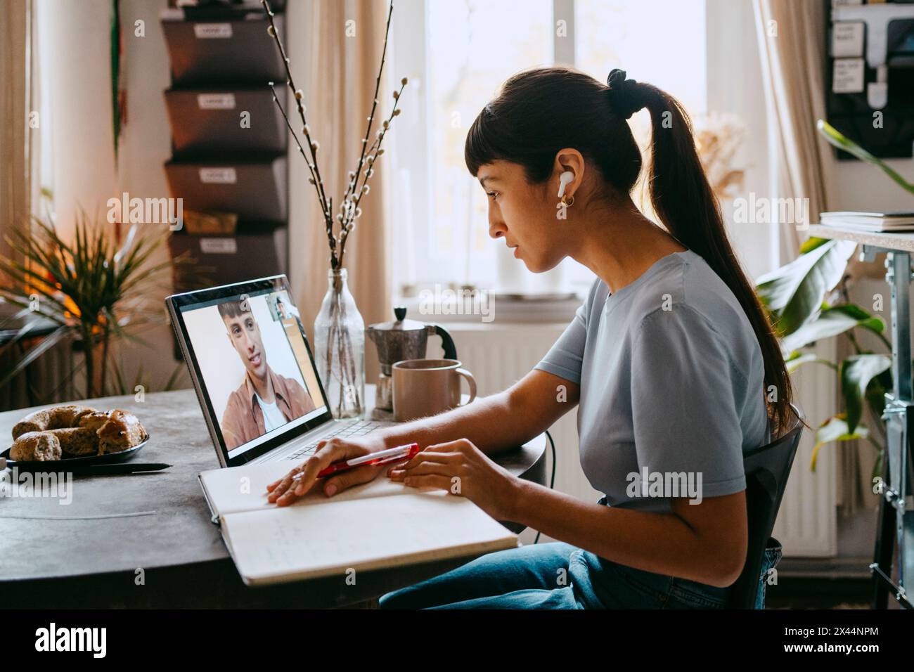 Vue latérale d'une femme indépendante faisant un appel vidéo avec un collègue masculin via un ordinateur portable au bureau à domicile Banque D'Images