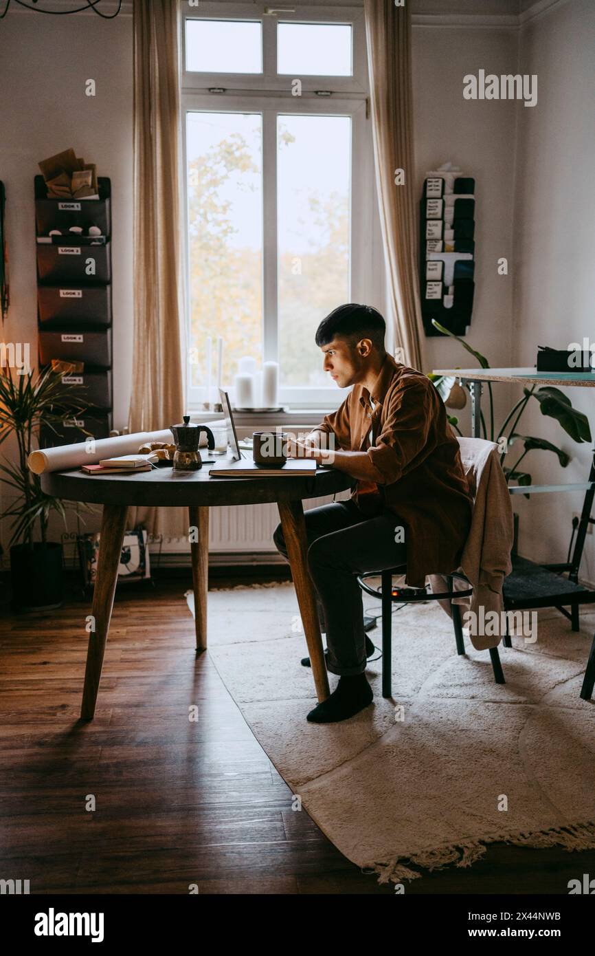 Jeune homme indépendant travaillant sur ordinateur portable tout en étant assis au bureau à domicile Banque D'Images