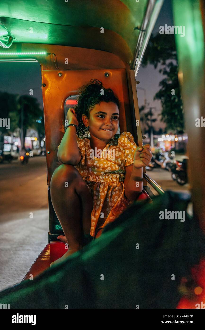 Fille souriante assise en tuk-tuk la nuit en ville Banque D'Images