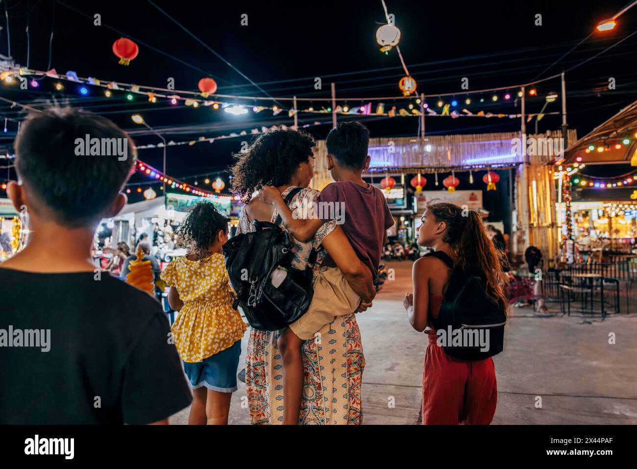 Vue arrière d'une femme explorant le marché alimentaire avec des enfants en vacances la nuit Banque D'Images
