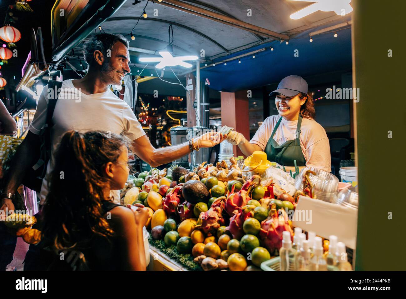 Homme souriant payant pour le jus tout en se tenant à l'étal dans le marché alimentaire Banque D'Images