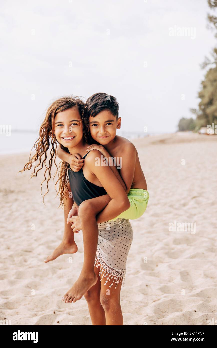 Portrait de fille souriante piggybackBrother tout en se tenant sur le sable à la plage Banque D'Images