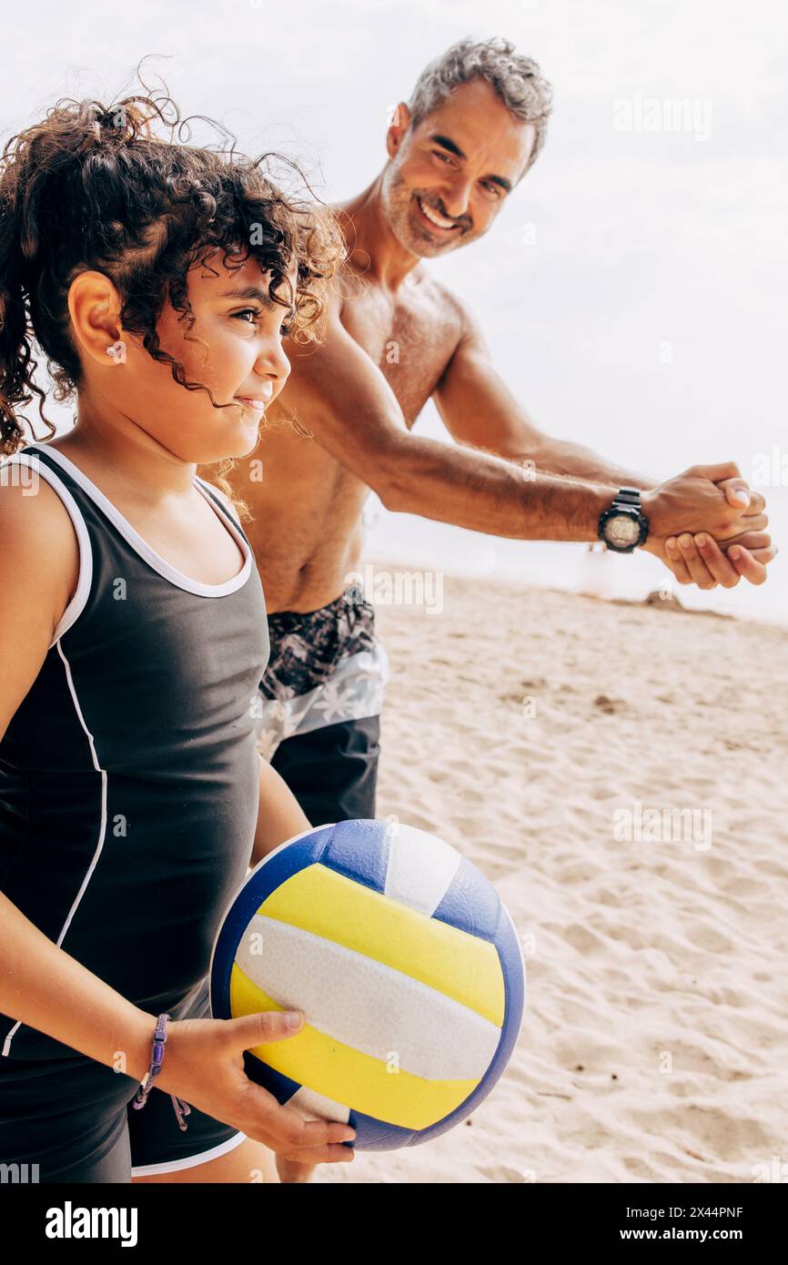 Homme souriant enseignant le service de flotteur à sa fille tenant le volley à la plage Banque D'Images
