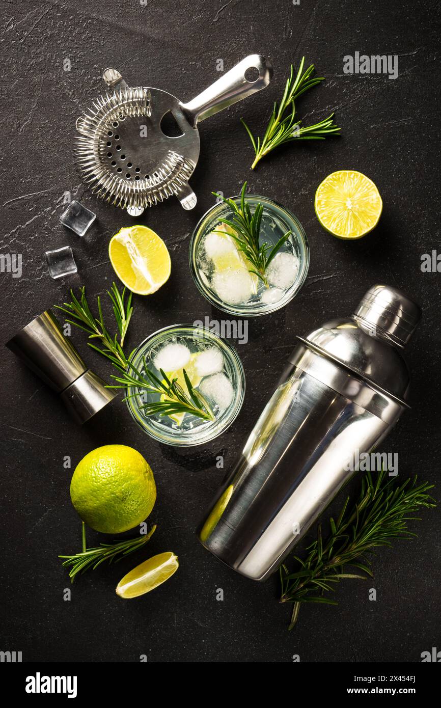 Gin tonic, cocktail traditionnel avec gin, tonic, glaçons, citron vert et romarin sur fond noir. Vue de dessus. Banque D'Images