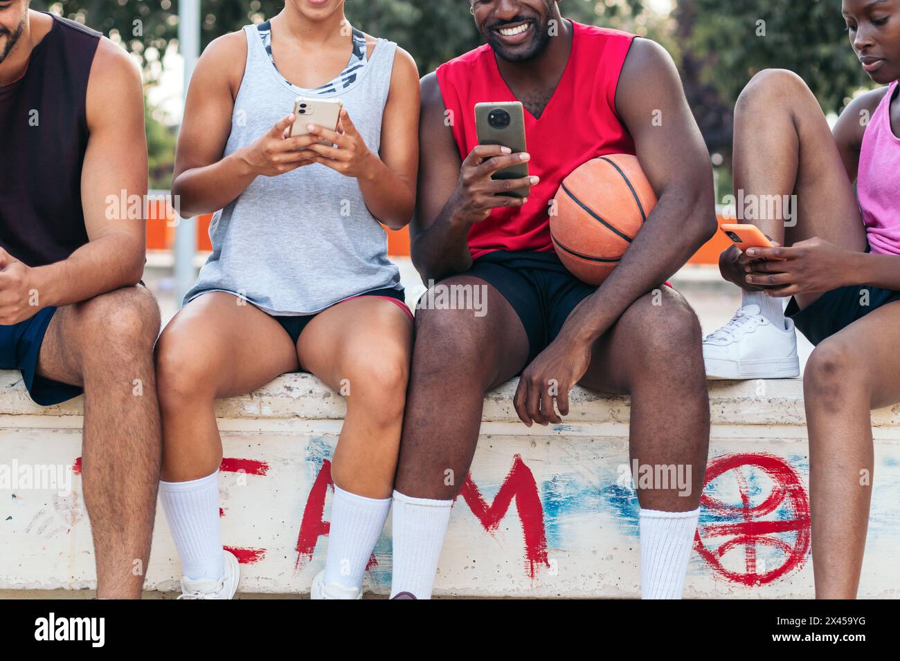 Groupe d'amis multiraciaux utilisant un smartphone après un match de basket-ball Banque D'Images