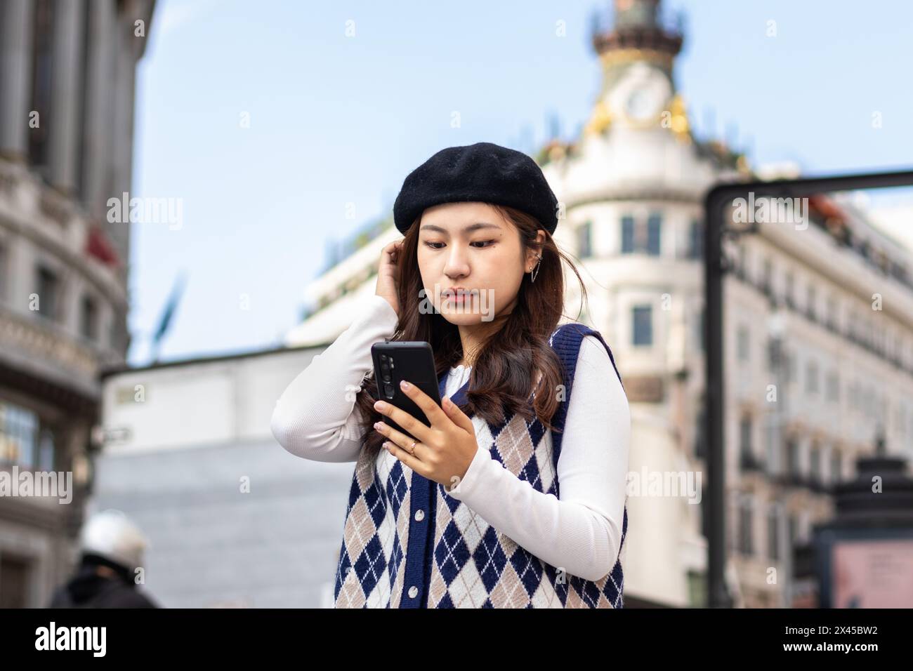 Jeune femme chinoise adulte dans des vêtements de mode à l'aide d'un smartphone dans les rues d'une ville européenne Banque D'Images