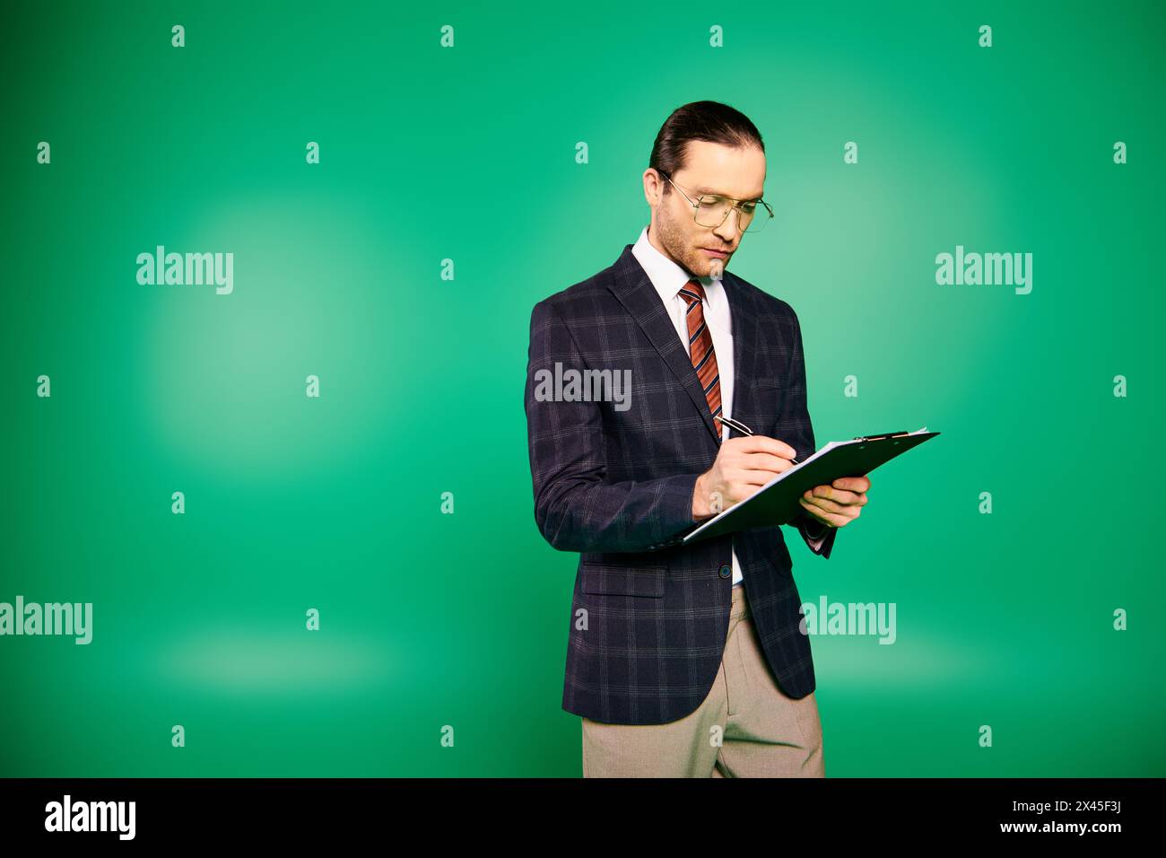 Bel homme d'affaires dans un costume chic et cravate, tenant un presse-papiers sur un fond vert. Banque D'Images