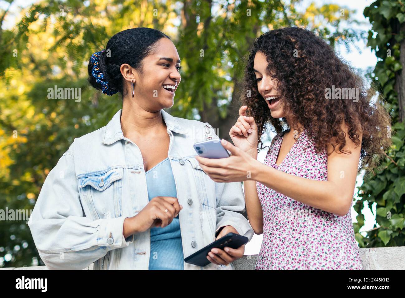 Deux amis latino-américains marchant dans la rue, s'amusant et riant en utilisant un smartphone. Banque D'Images