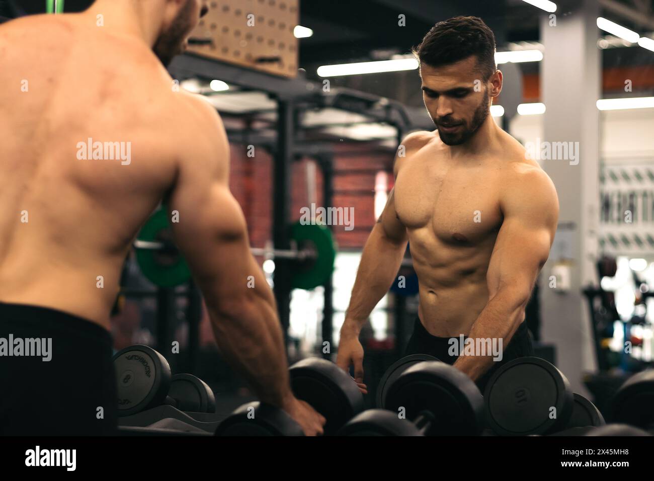 homme fort debout devant le miroir prenant des haltères dans une salle de gym Banque D'Images