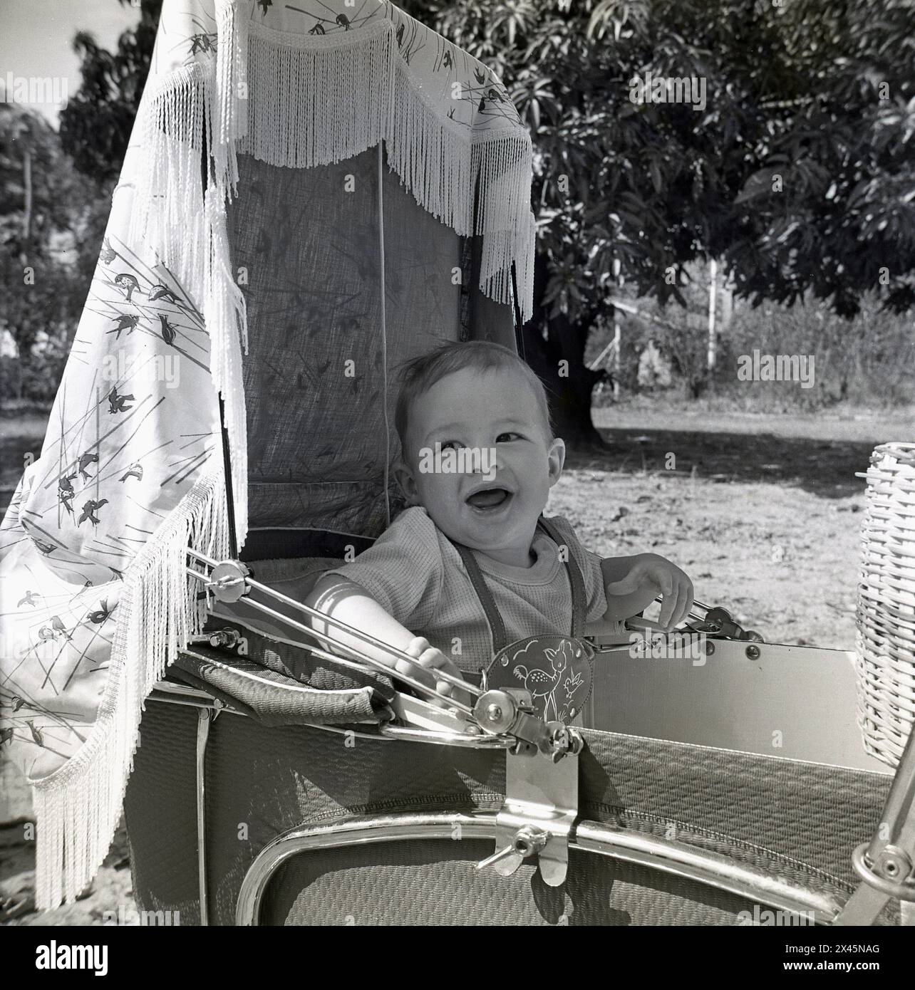 années 1960, historique, un enfant en bas âge assis dans une poussette, à l'ombre, attaché avec un harnais de sécurité en cuir. Banque D'Images