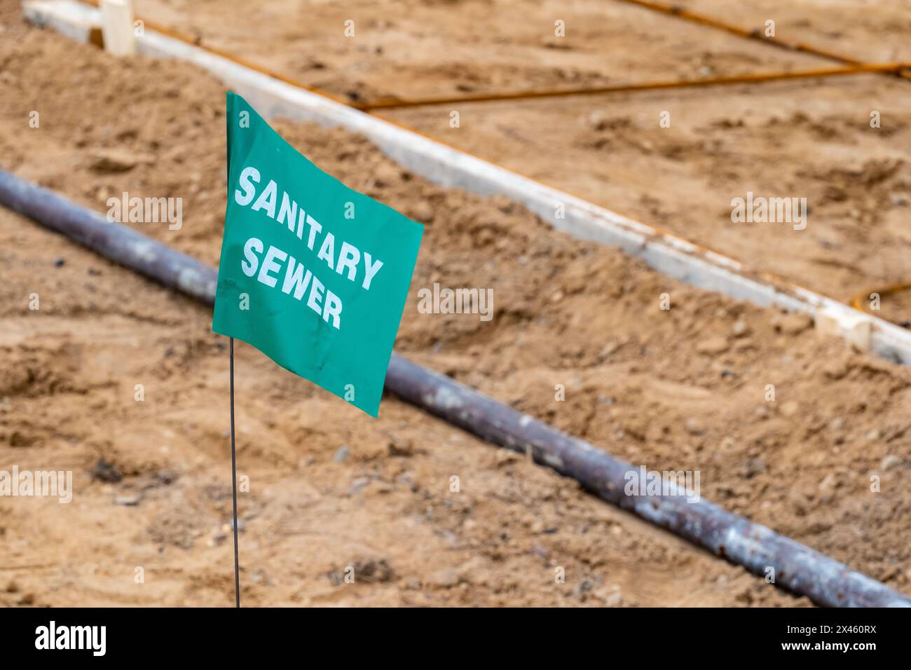 Petit drapeau vert avec lettrage blanc, avertissant d'une conduite d'égout sanitaire souterraine, sur un nouveau chantier de construction de maison. Banque D'Images