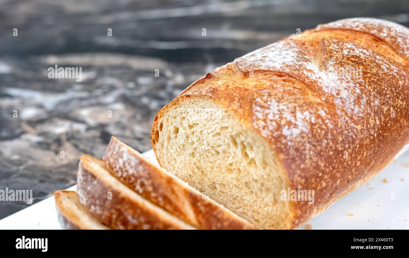 Gros plan d'une miche partiellement tranchée de pain de blé artisanal fait maison, avec une croûte croquante et une miette ouverte. Profondeur de champ limitée sélective de mise au point. Bruit g Banque D'Images
