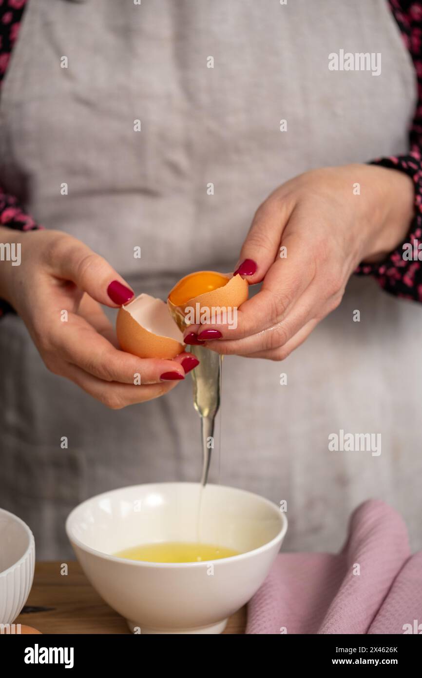 Gros plan des mains craquant habilement un œuf, le jaune se séparant du blanc dans un bol, une technique fondamentale dans la préparation culinaire. Qu. Élevé Banque D'Images