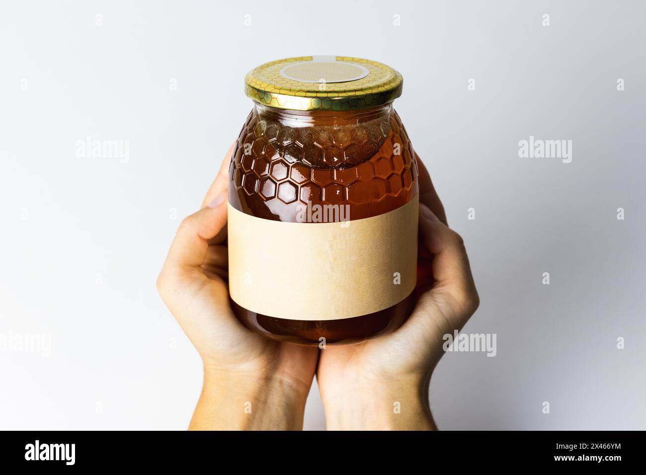Crop-personne méconnaissable avec miel liquide naturel dans un pot en verre sur fond blanc Banque D'Images