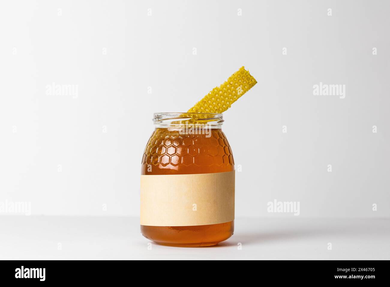 Morceau de nid d'abeille sur le dessus du pot en verre plein de miel doré naturel frais avec fond blanc Banque D'Images