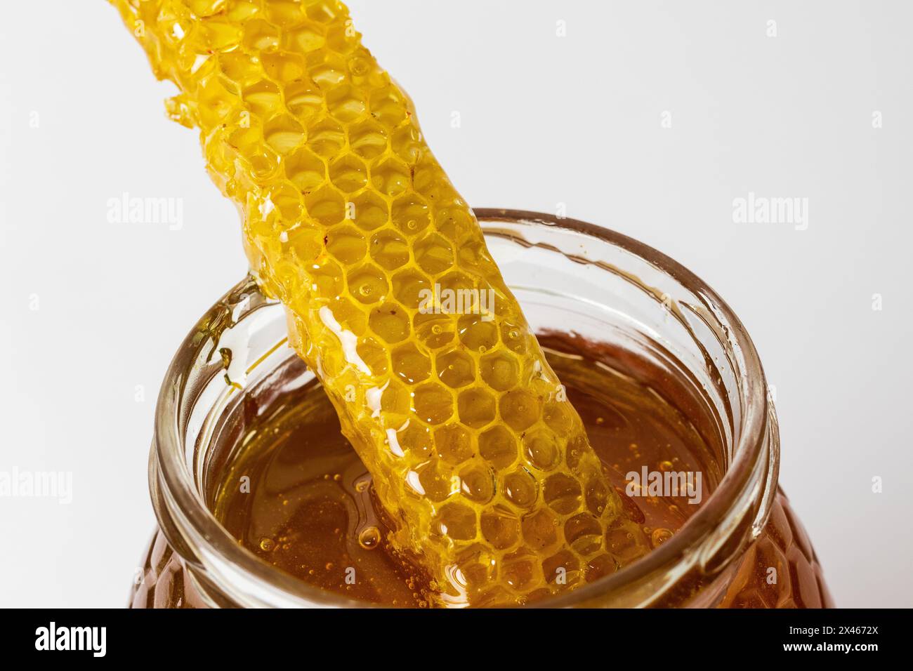 Gros plan d'un morceau de nid d'abeille sur le dessus du pot en verre plein de miel doré naturel frais avec fond blanc Banque D'Images