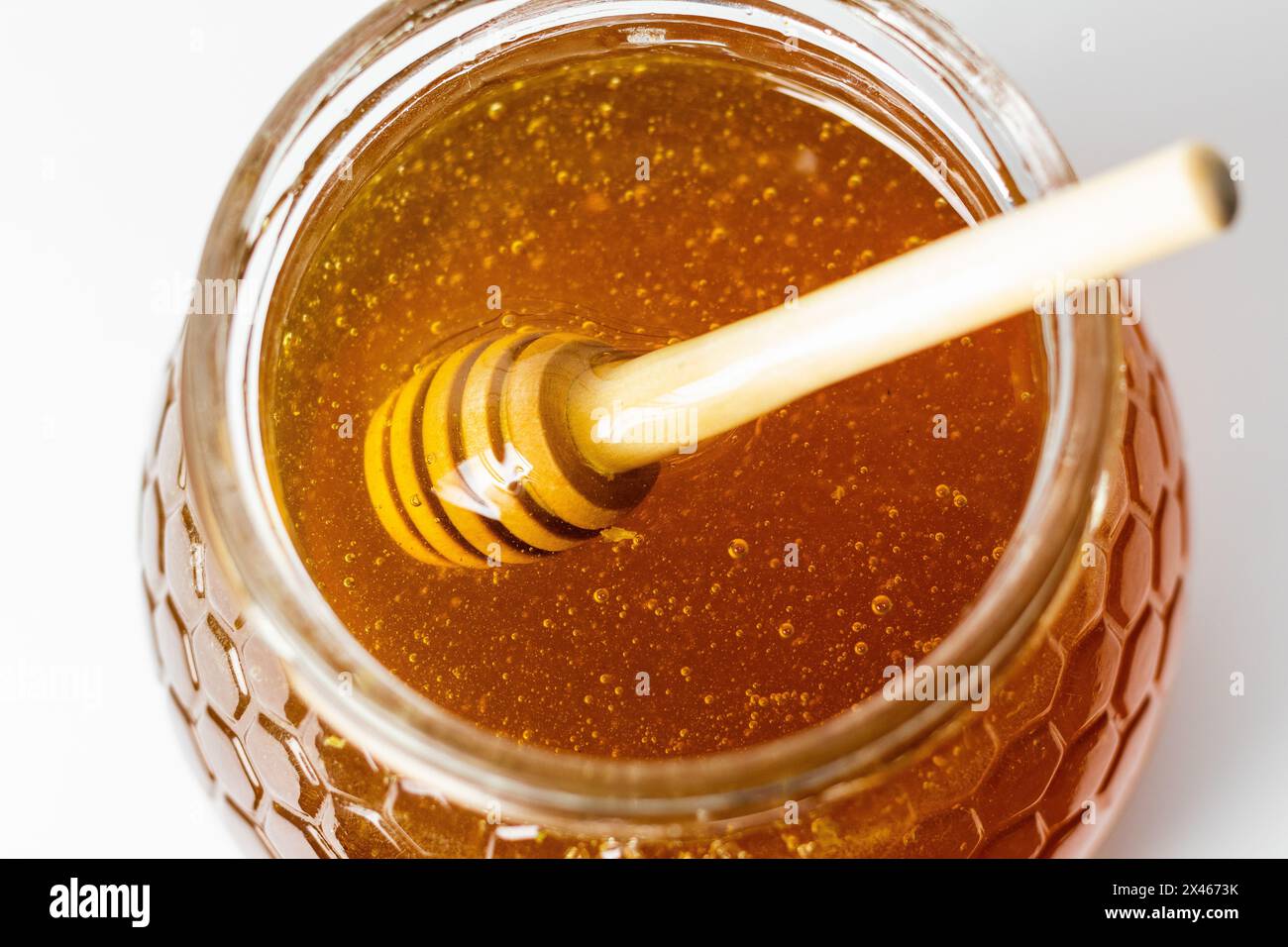 De dessus de gros plan du balancier en remuant le miel doré aromatique frais dans un bol en verre Banque D'Images