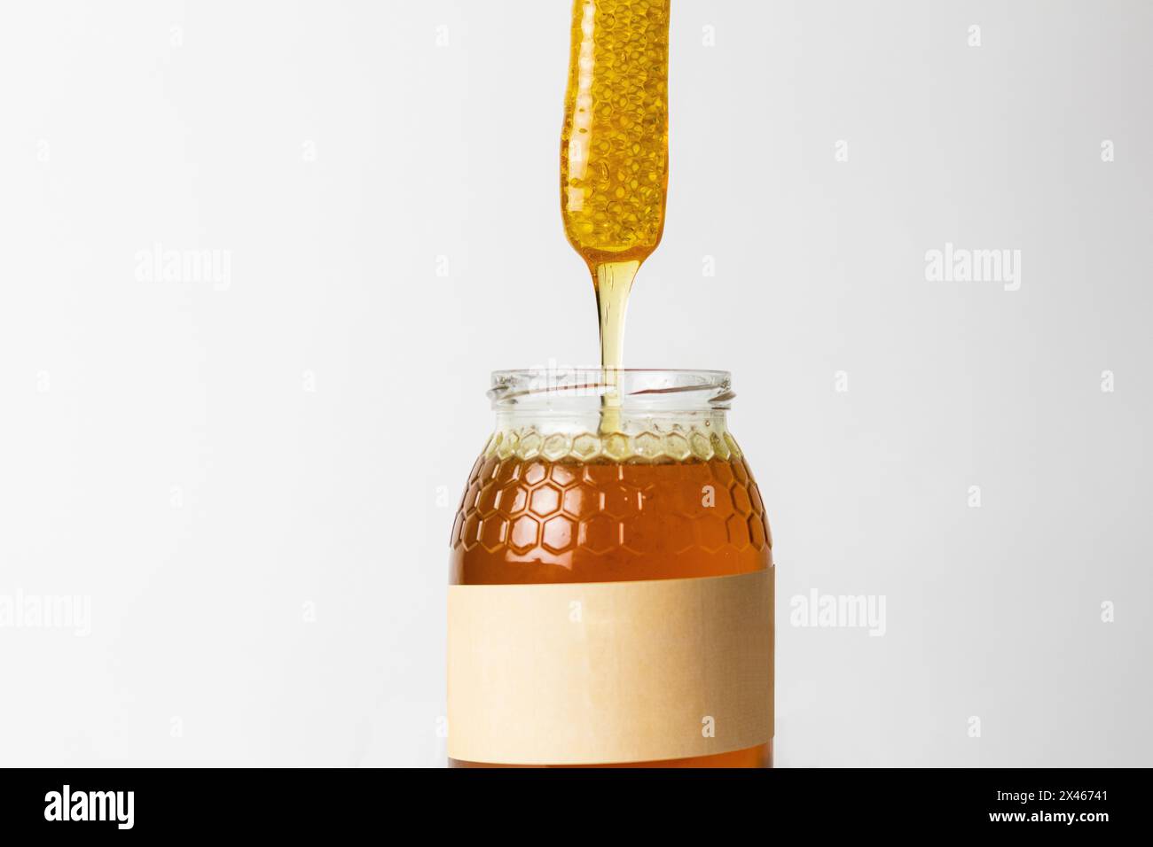 Morceau de nid d'abeille sur le dessus du pot en verre plein de miel doré naturel frais avec fond blanc Banque D'Images