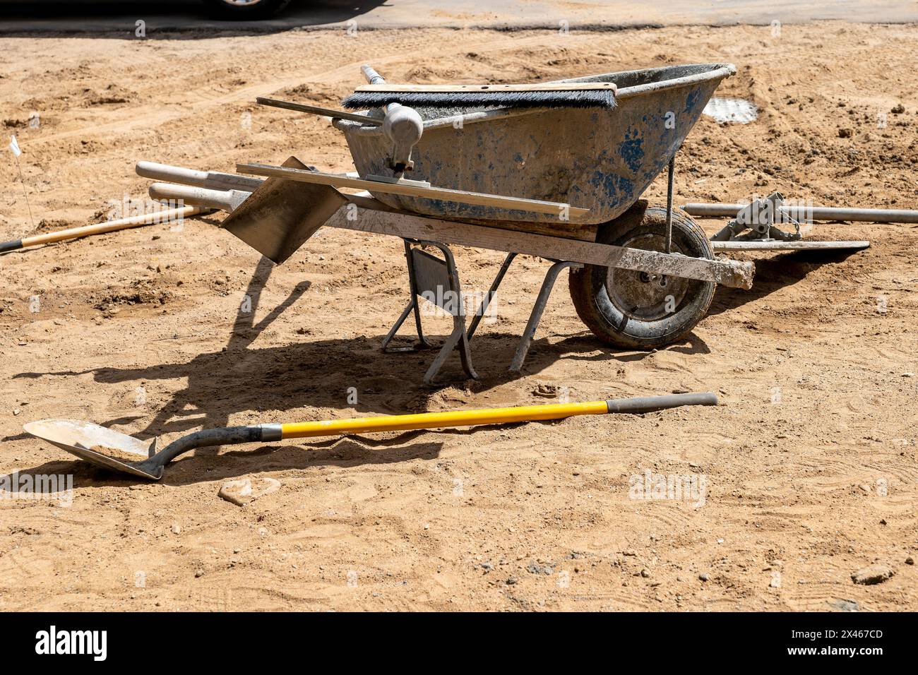 Une brouette de roue sale et d'autres outils, utilisés par un constructeur pour faire un trottoir en béton sur un chantier de construction. Banque D'Images