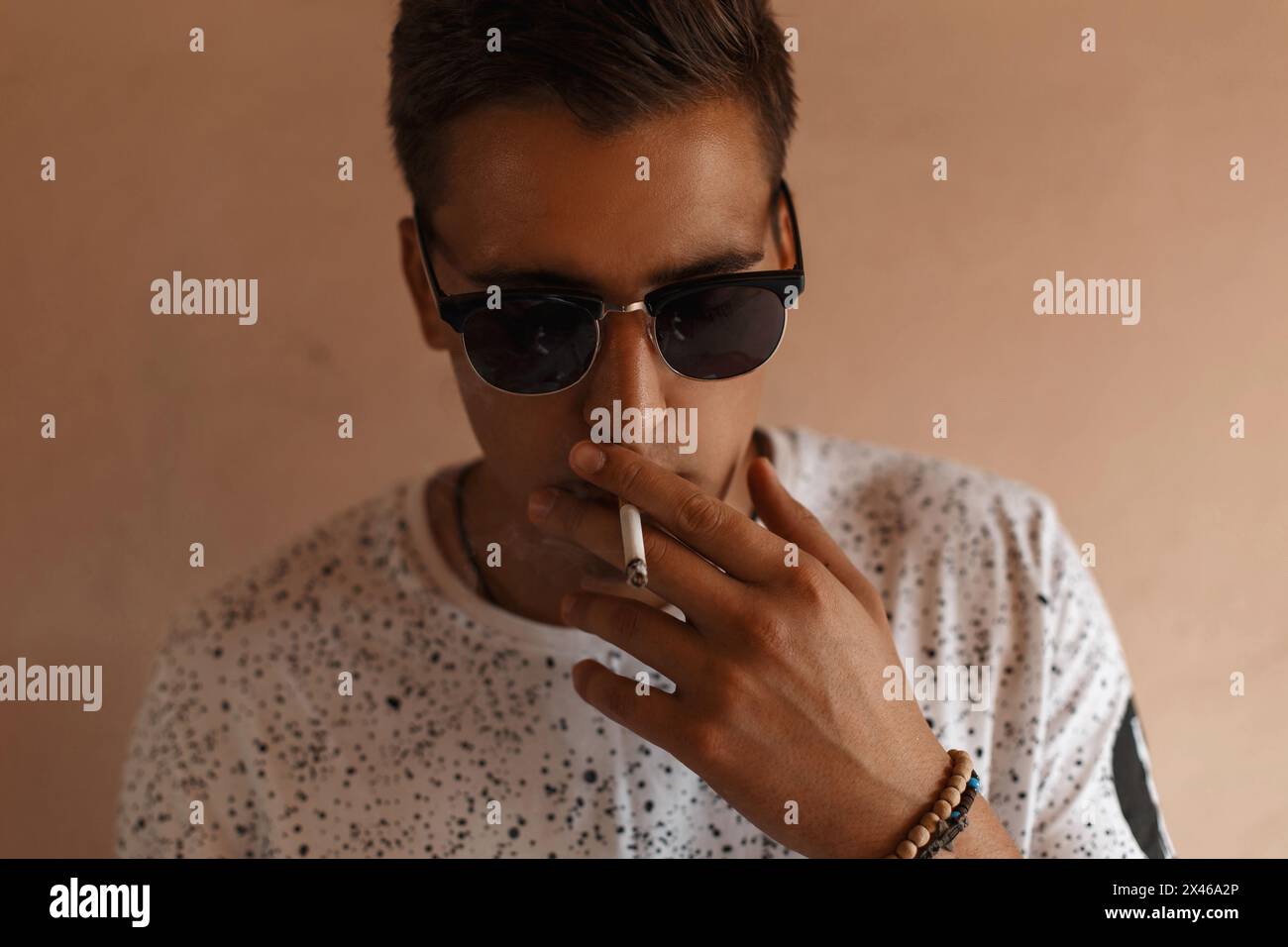 Jeune homme hipster avec lunettes de soleil et coiffure fumant Une cigarette. Banque D'Images