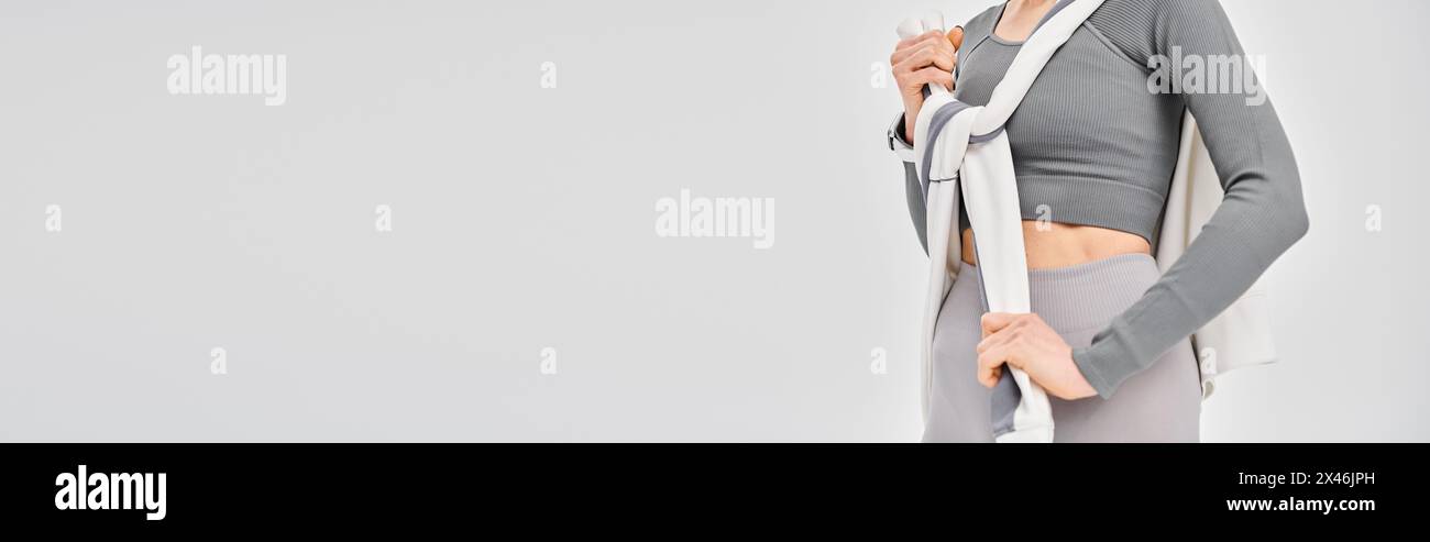 Une jeune femme sportive montrant sa tenue athlétique avec confiance sur un fond gris. Banque D'Images
