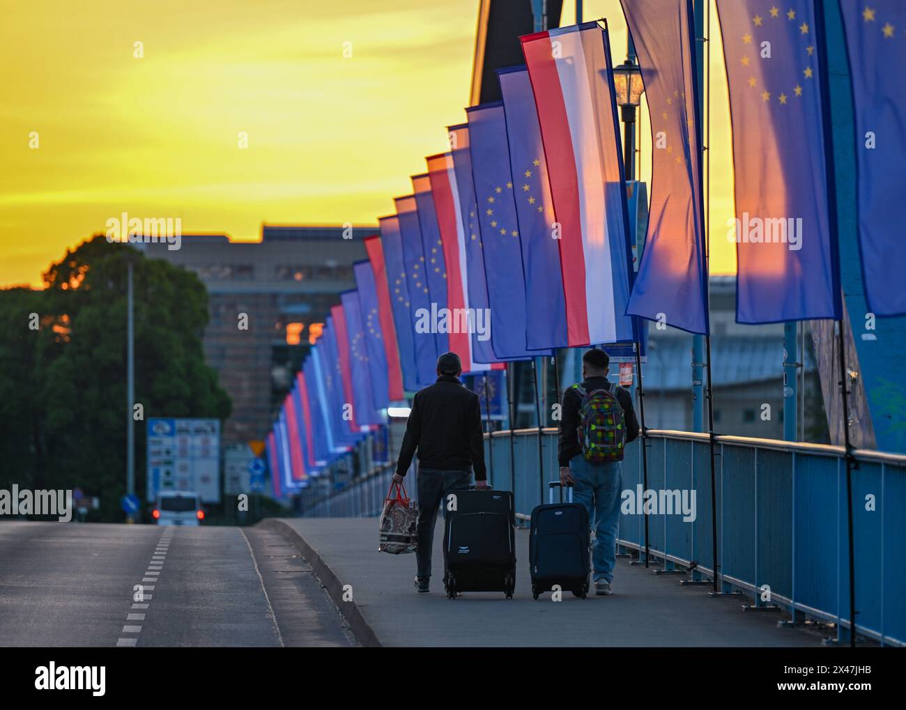 01 mai 2024, Brandebourg, Francfort (Oder) : deux voyageurs traversent le pont de la ville au-dessus de la rivière frontalière Oder entre Francfort (Oder) et Slubice en Pologne au lever du soleil. Les ministres des Affaires étrangères des deux pays voisins souhaitent se réunir à midi pour marquer le 20e anniversaire de l'adhésion de la Pologne à l'UE. Les deux veulent visiter le Collegium Polonicum à Slubice du côté polonais, ainsi qu'un festival européen, puis traverser ensemble le pont de la ville sur la frontière germano-polonaise de l'Oder à Francfort (Oder). Photo : Patrick Pleul/dpa Banque D'Images