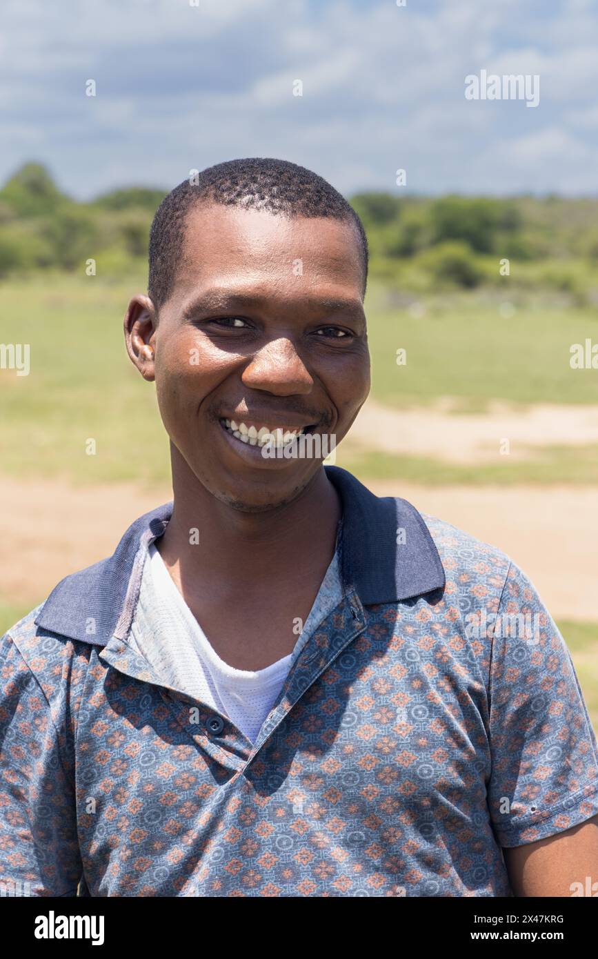 village célibataire jeune homme africain avec un sourire dentelé, à l'extérieur dans la nature dans un champ vert Banque D'Images