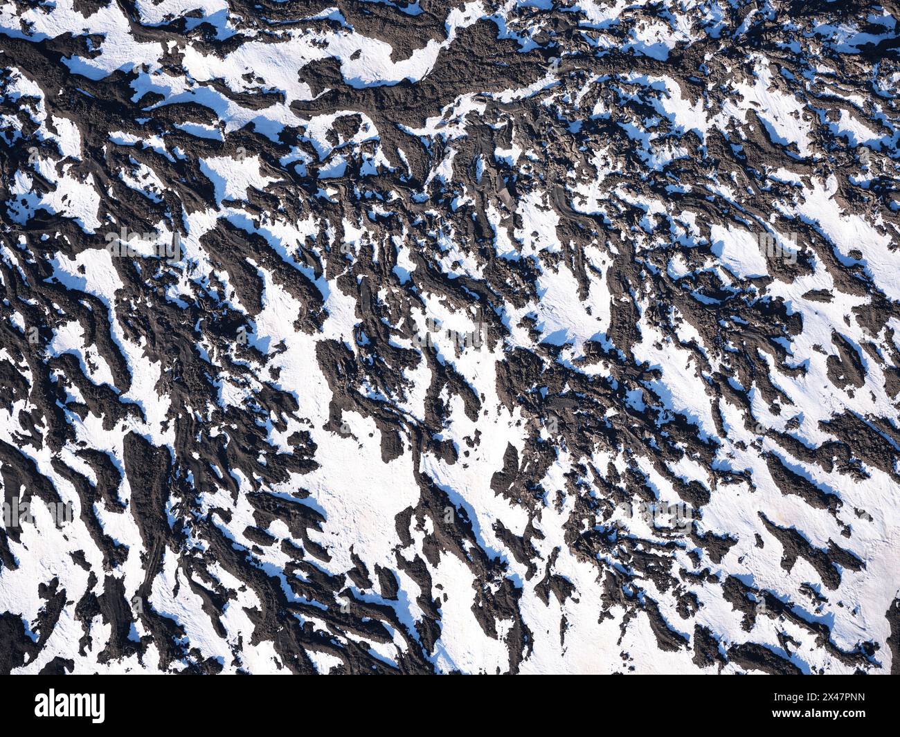 VUE AÉRIENNE. La neige de printemps et la lave coulent sur le versant nord de l'Etna. Ville métropolitaine de Catane, Sicile, Italie. Banque D'Images
