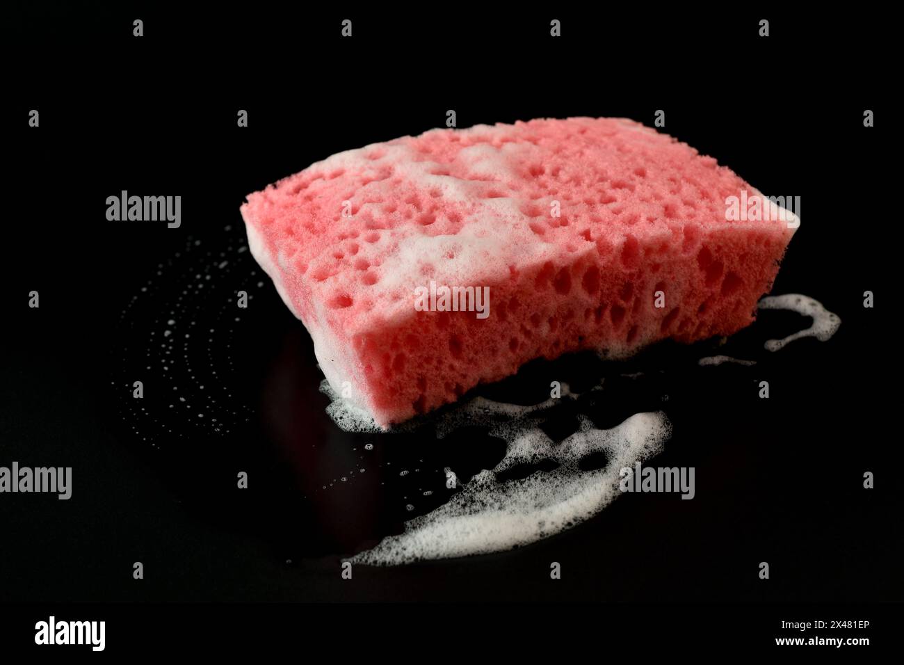 Sur fond noir, une éponge à vaisselle rouge avec mousse de savon blanche. Banque D'Images