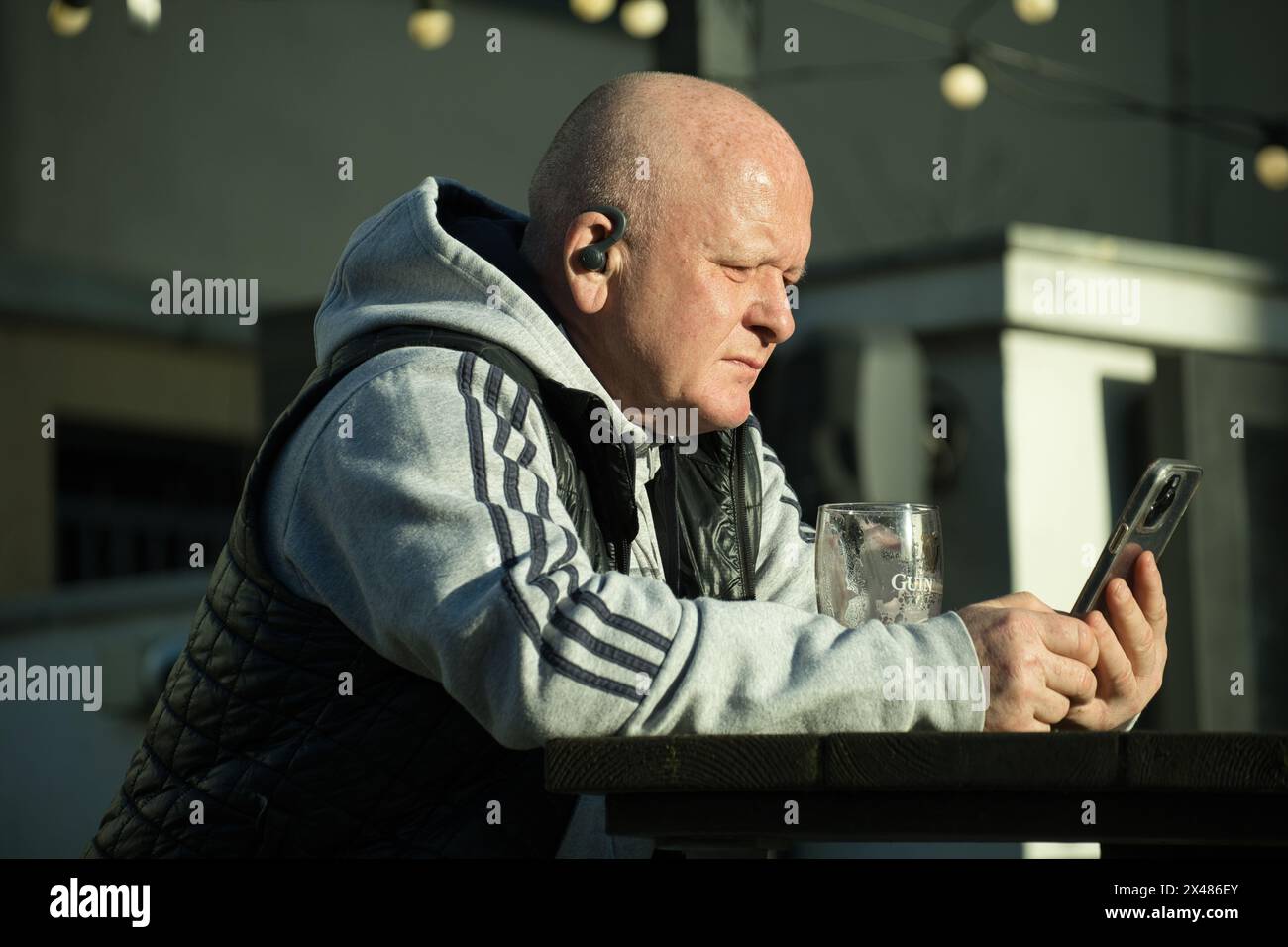 Homme chauve d'âge moyen devant un pub sur son téléphone portable Banque D'Images