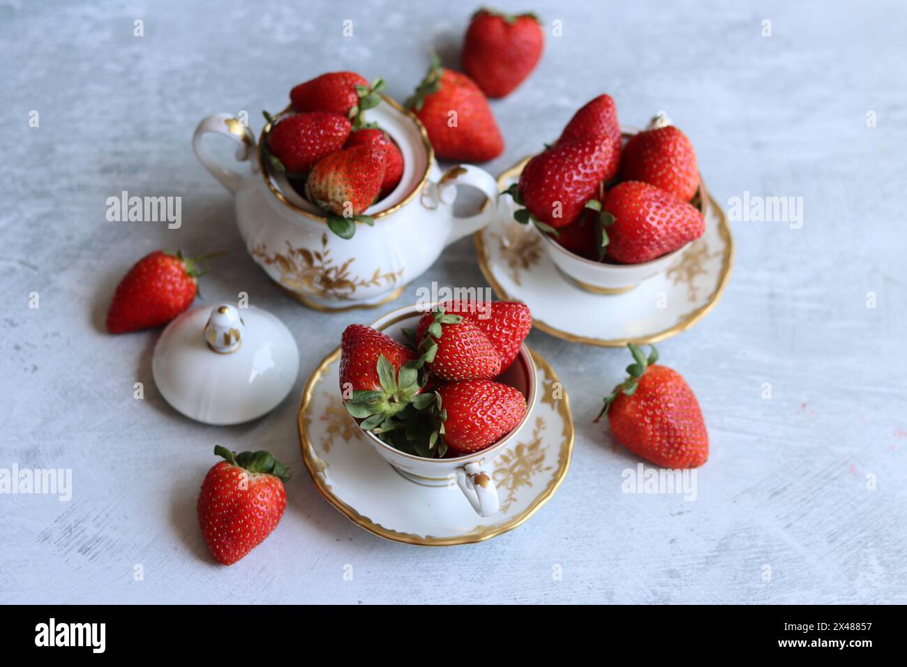 Fraises dans une tasse en porcelaine de style rétro blanc sur fond texturé gris clair avec espace pour le texte. Fruits biologiques de saison estivale. Manger frais. Banque D'Images