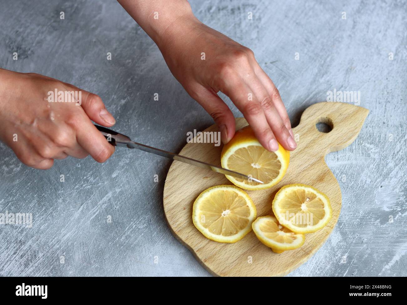 Les mains féminines coupent des citrons sur une planche de bois sur un fond gris avec un espace pour le texte Banque D'Images