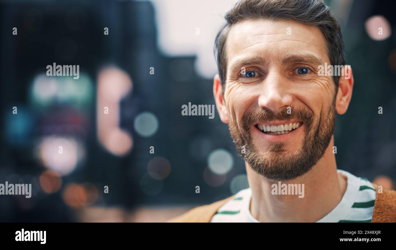 Portrait d'un heureux bel homme Bearded dans des vêtements décontractés debout dans la rue regardant caméra, souriant. Élégant jeune adulte ou homme d'âge moyen avec barbe. Blurred Dig City en arrière-plan Banque D'Images