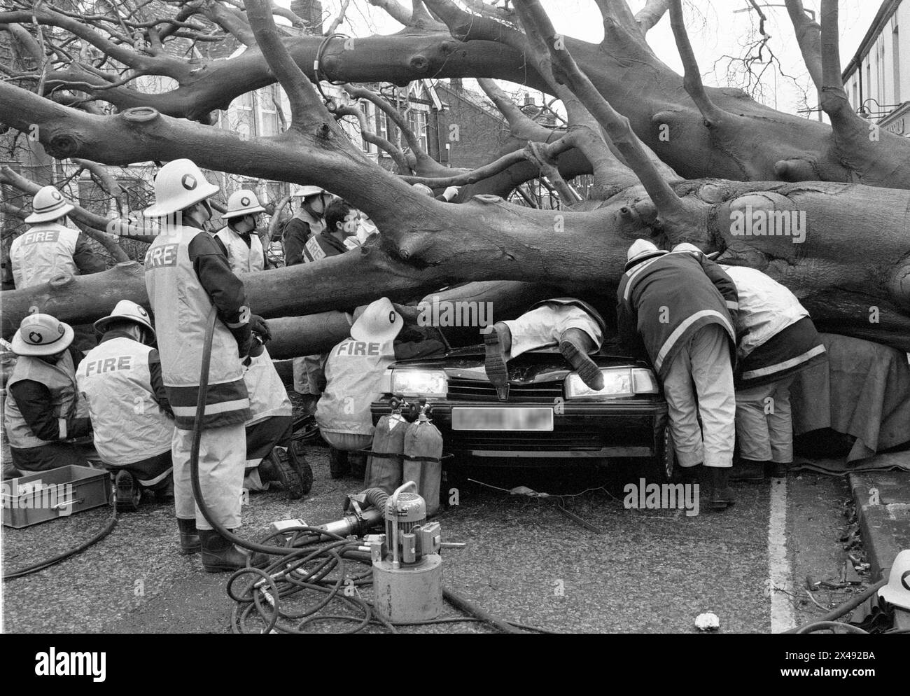Une image de journal d'archives de pompiers et Poilce se précipitant pour sauver un conducteur dans une voiture partiellement écrasée sous un arbre tombé pendant la grande tempête de janvier 1990. Banque D'Images