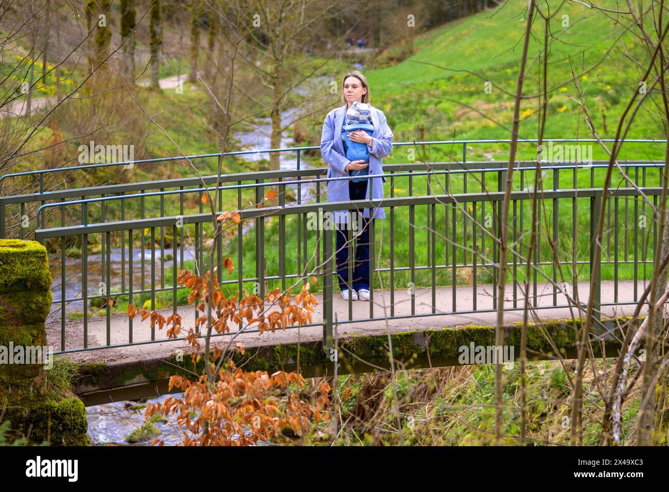 Belle femme blonde debout sur un pont dans la nature avec son petit bébé Banque D'Images